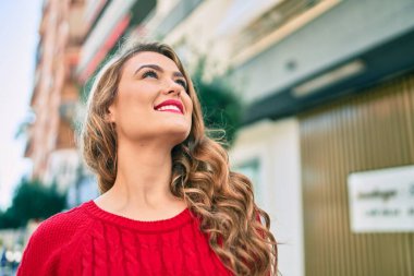 Genç sarışın kız gülümseyerek şehirde mutlu mesut yürüyor..