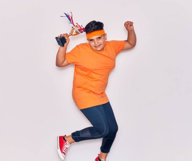 Spor kıyafetleri giyen sevimli İspanyol çocuk mutlu gülümsüyor. Yüzünde tebessümle zıplıyor İzole edilmiş beyaz arka planda ödül tutuyordu