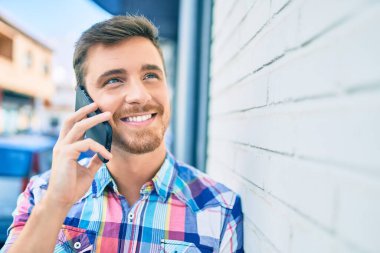 Genç beyaz adam gülümsüyor. Şehirdeki akıllı telefondan konuşuyor..