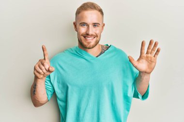 Gündelik giysiler giymiş genç beyaz bir adam altı numarayı gösterip işaret ederken kendinden emin ve mutlu bir şekilde gülümsüyor.. 
