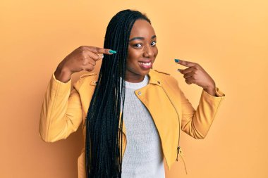 Rahat bir ceket giyen, neşeli gülümseyen ve parmaklarıyla ve ağzıyla işaret eden genç Afrikalı Amerikalı kadın. diş sağlığı kavramı. 