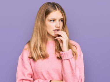 Gündelik kazak giyen güzel, genç, beyaz bir kız. Ağzı tırnak yiyen ellerle stresli ve gergin görünüyor. anksiyete. 