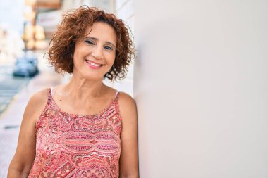 Orta yaşlı kadın gülümsüyor. Şehrin duvarına yaslanmış mutlu bir şekilde..