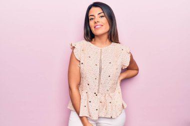 Genç, güzel, esmer, sıradan kıyafetler giyen mutlu ve kendinden emin bir kadın. İzole edilmiş pembe arka planda yüzünde bir gülümsemeyle duruyorum.