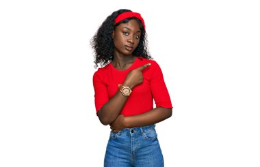 Güzel Afrikalı genç bir kadın, gündelik giysiler giyip, el parmaklarıyla kenarı işaret ederek ciddi ve sakin bir yüz ifadesi sergiliyor. 