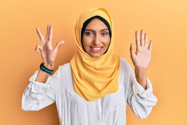Genç esmer Arap kadın geleneksel başörtüsü takıyor dokuz numarayı gösterip gösterirken kendinden emin ve mutlu gülümsüyor.. 