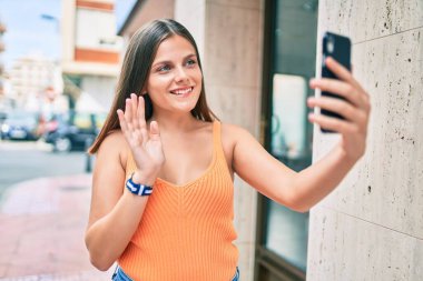 Ortadoğulu genç bir kız şehirde akıllı telefon kullanarak video araması yaparken mutlu gülümsüyor..