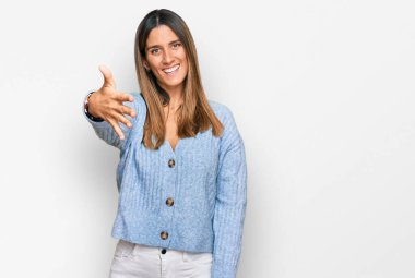 Günlük kıyafetler giyen genç bir kadın gülümseyerek selamlama ve hoş geldin demek için tokalaşmayı teklif ediyor. başarılı iş. 