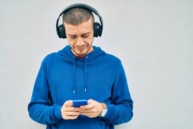 Şehirde akıllı telefon ve kulaklık kullanan ciddi bir suratı olan genç bir İspanyol..