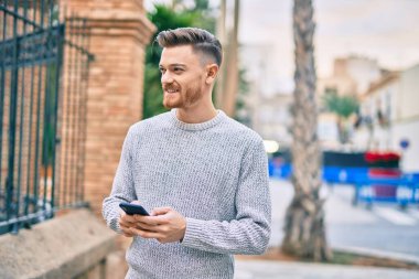 Beyaz adam şehirde akıllı telefon kullanarak mutlu bir şekilde gülümsüyor..
