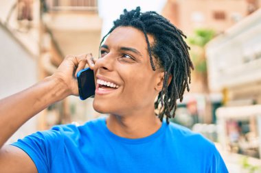 Genç Afrikalı Amerikalı gülümseyen mutlu bir adam şehrin caddesinde akıllı telefondan konuşuyor..