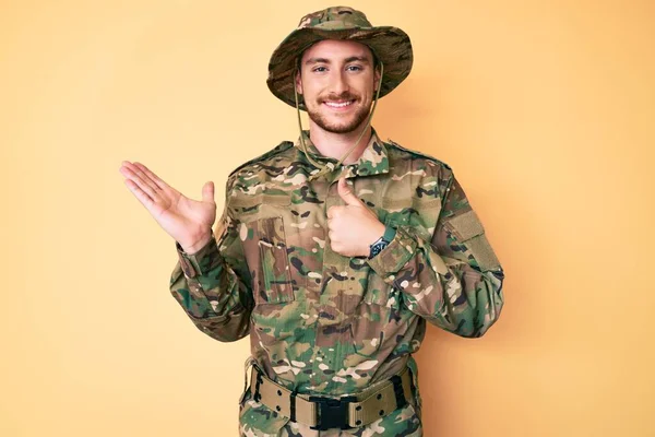 若いです白人男性を身に着けていますカモフラージュ軍制服手のひらの手を示すと親指でOkジェスチャーを行います 笑顔幸せと陽気な — ストック写真