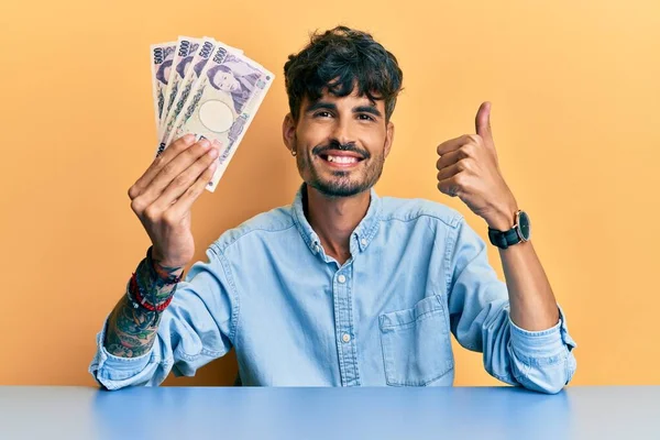 Young Hispanic Man Holding Japanese Yen Banknotes Sitting Table Smiling — Fotografia de Stock