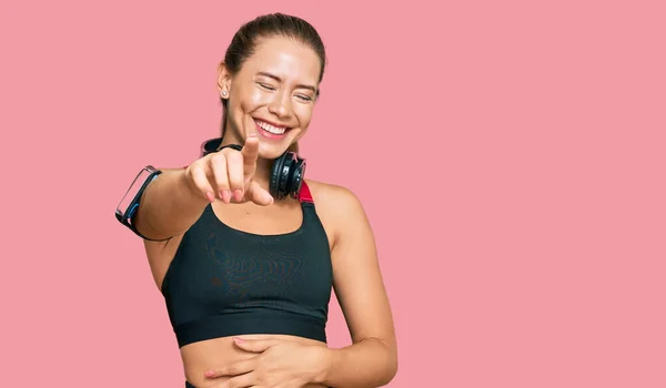 Hermosa Mujer Rubia Vistiendo Ropa Gimnasio Usando Auriculares Riéndose Señalando —  Fotos de Stock