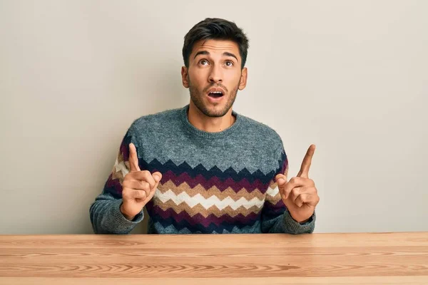 Joven Hombre Guapo Con Suéter Casual Sentado Mesa Sorprendido Sorprendido — Foto de Stock