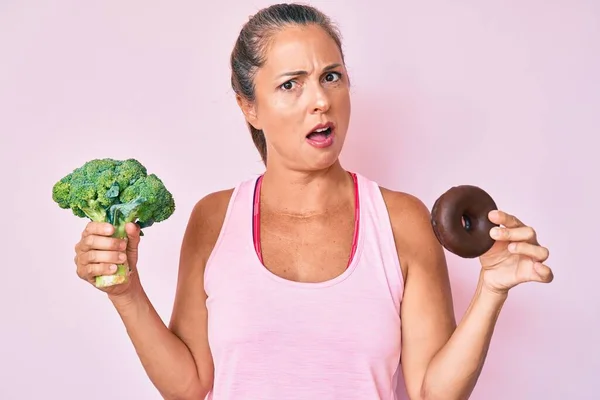 中年时 他惊慌失措的女人带着花椰菜和巧克力甜甜圈 脸上带着震惊的表情 脸上带着怀疑和讽刺的表情 张大了嘴 吃惊极了 — 图库照片