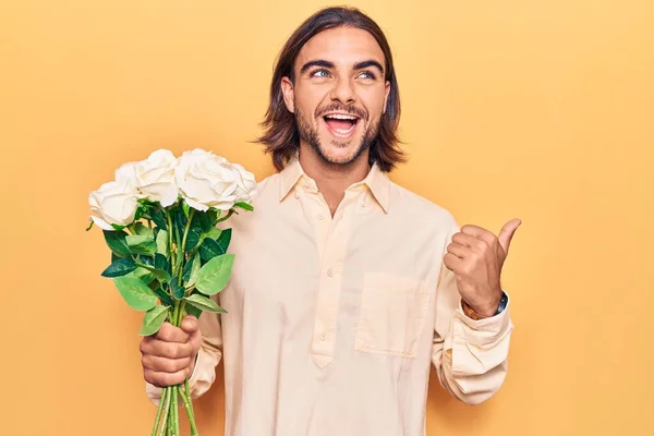 Joven Hombre Guapo Sosteniendo Flores Apuntando Con Pulgar Hacia Lado — Foto de Stock