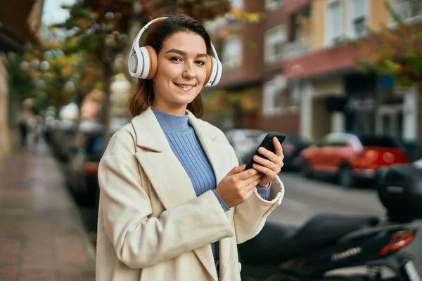 街中でスマホやヘッドフォンを使って笑顔で幸せそうな若いヒスパニック系女性 — ストック写真