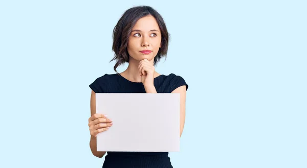 Young Beautiful Girl Holding Blank Empty Banner Serious Face Thinking — Stock Photo, Image