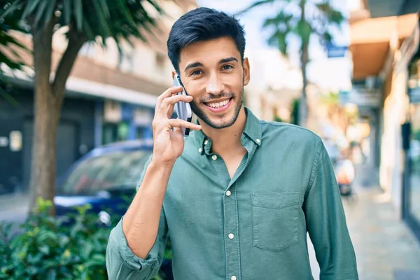 年轻的拉丁裔男子笑着高兴地在城市里用智能手机交谈 — 图库照片