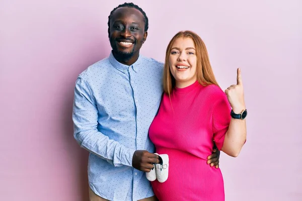 Young Interracial Couple Expecting Baby Holding Shoes Smiling Idea Question — Stock Photo, Image