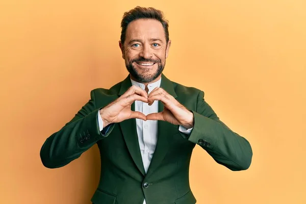 Middle age man wearing business suit smiling in love doing heart symbol shape with hands. romantic concept.