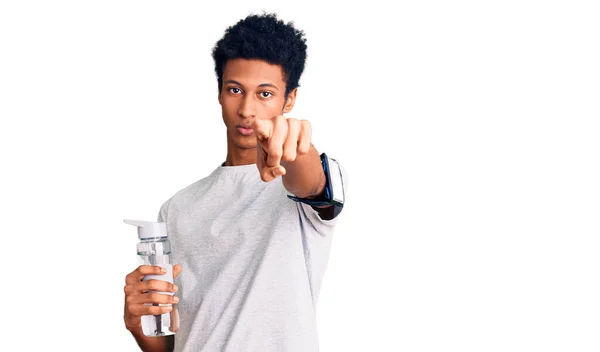 若いアフリカ系アメリカ人の男を着てスポーツウェアを保持水ボトルを指差す指でカメラとあなたに 自信を持ってジェスチャーを真剣に見て — ストック写真