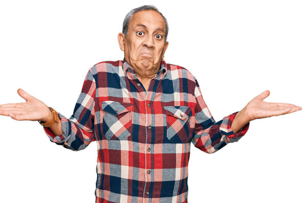 Senior hispanic man wearing casual clothes clueless and confused expression with arms and hands raised. doubt concept. 