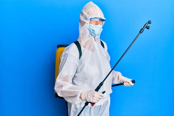 Covid specialist wearing decontamination protective suit and disinfectant spray, decontaminate and sanitize surface, standing over blue background