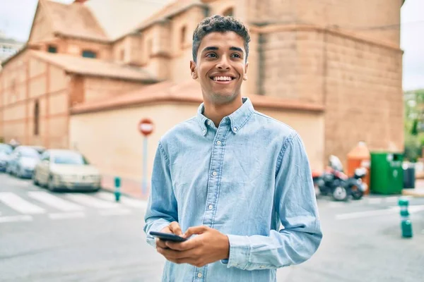 若いラテン語の男笑顔幸せな使用してスマートフォン街を歩く — ストック写真