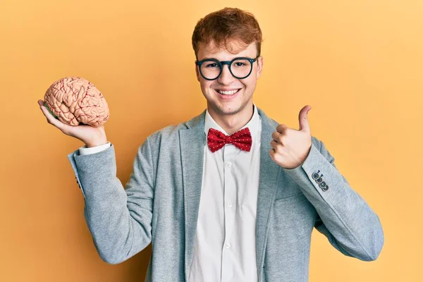 Jovem Caucasiano Vestindo Óculos Segurando Cérebro Sorrindo Feliz Positivo Polegar — Fotografia de Stock