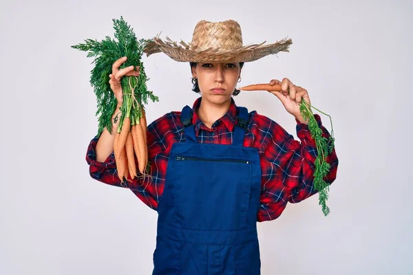 Hermosa Mujer Morena Vistiendo Ropa Granjero Sosteniendo Zanahorias Frescas Escéptico — Foto de Stock