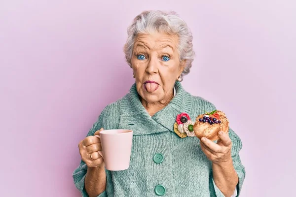 先輩の白髪の女がコーヒーを飲みながら舌を出して食べる面白い表情で幸せ — ストック写真