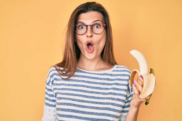 美丽的高加索女人把吃香蕉当作健康的小吃 吓着了 惊讶得张大了嘴 惊讶得面目全非 — 图库照片
