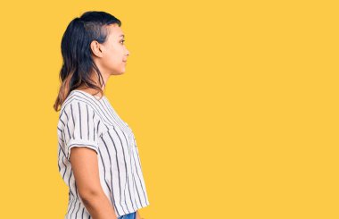 Sıradan kıyafetler giyen genç bir kadın, rahat bir görünüm takınıyor, doğal bir yüz ve kendine güvenen bir gülümsemeyle poz veriyor.. 