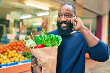 Elinde süpermarketten alınmış kağıt torba sakallı Afrikalı Amerikalı adam telefonda konuşuyor.
