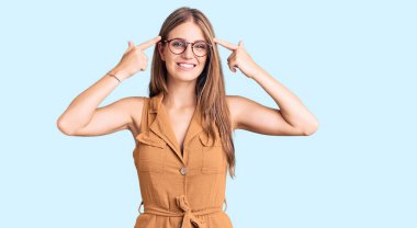 Young beautiful blonde woman wearing casual clothes and glasses smiling pointing to head with both hands finger, great idea or thought, good memory 