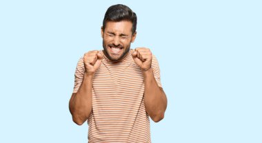 Başarılı olmak için heyecanlı, kolları havada ve gözleri kapalı, sıradan kıyafetler giyen yakışıklı İspanyol adam zaferi kutluyor. Kazanan konsept. 