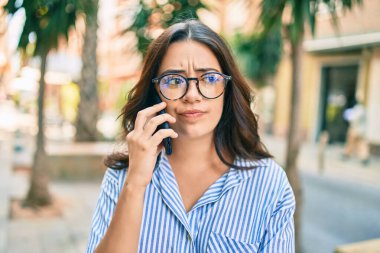 Endişeli yüzüyle şehirde akıllı telefondan konuşan genç İspanyol iş kadını..