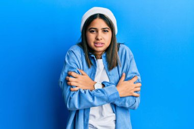 Tatlı yün şapka takan genç Latin kadın kış soğuğu için titriyor ve donuyor. Yüzünde üzgün ve şok ifadesi var. 