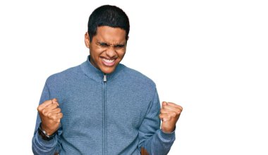 Genç, yakışıklı, sıradan bir tişört giyen, mutlu ve heyecanlı, kolları havada, gülümseyen ve başarı için bağıran, kazanan bir jest yapan İspanyol. kutlama konsepti. 