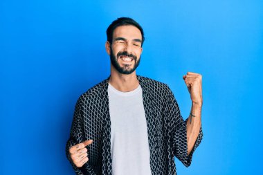 Gündelik giysiler giyen genç İspanyol adam şaşkınlık ve şaşkınlık içinde kollarını kaldırarak ve gözlerini kapayarak başarıyı kutluyor. 