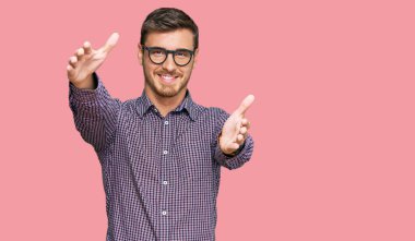 Sıradan kıyafetler ve gözlük takan yakışıklı beyaz adam kucaklaşmak için kollarını açmış kameraya bakıyor. Mutluluğu kucaklayan neşeli bir ifade.. 