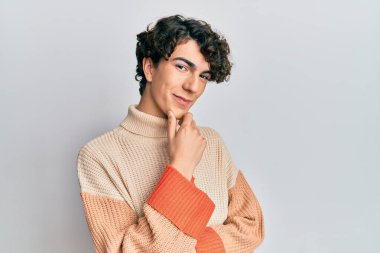 Sıradan bir kazak giyen İspanyol genç adam kameraya kollarını kavuşturup gülümseyerek ve çenesini kaldırarak bakıyor. Olumlu düşünmek. 