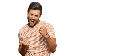 Gündelik kıyafetler giyen yakışıklı İspanyol adam kolları havada ve gözleri kapalı bir şekilde başarıyı kutluyor ve şaşırıyor. Kazanan konsept. 