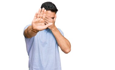 Latin kökenli genç bir adam, günlük kıyafetler giyip, elleriyle gözlerini kapatıyor ve üzgün ve korku ifadeleriyle jestleri durduruyor. utangaç ve olumsuz kavram. 