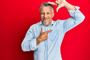 Orta yaşlı, gri saçlı, günlük kıyafetler giyen, gülümseyen, elleri ve parmakları mutlu yüzlü bir adam. yaratıcılık ve fotoğrafçılık kavramı. 