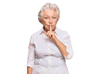 Gri saçlı, günlük kıyafetler giyen, dudakları parmaklı, sessiz olmak isteyen yaşlı bir kadın. sessizlik ve gizli konsept. 