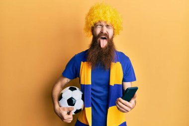 Kızıl saçlı, uzun sakallı futbol holigan amigoluk oyunu akıllı telefon tutan komik bir ifadeyle dilini dışarı çıkaran. 