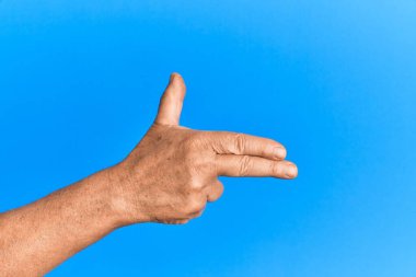 Mavi arka plandaki yaşlı İspanyol adamın eli parmaklarıyla ateşli silah doğrultuyor, nişan alıyor. 